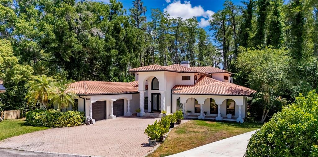 A two-story stucco house with a red tile roof and arched entryway sits in a forest — 17309 LINDA VISTA CIRCLE, LUTZ, FL