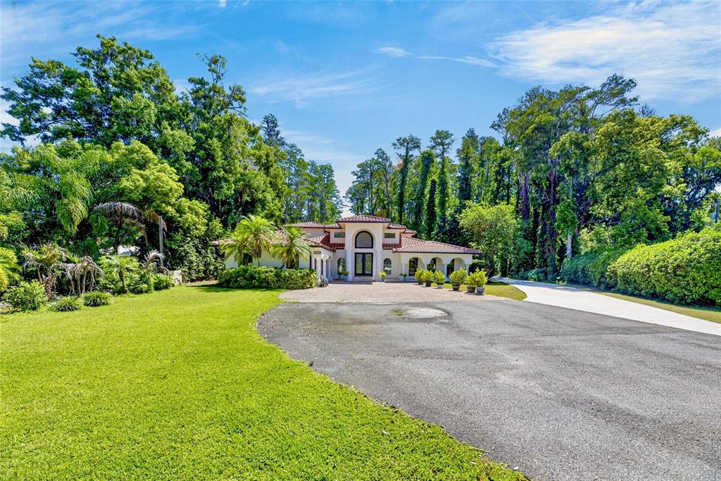 A single-story house with a tiled roof and arched entryway sits behind a large driveway — 17309 LINDA VISTA CIRCLE, LUTZ, FL