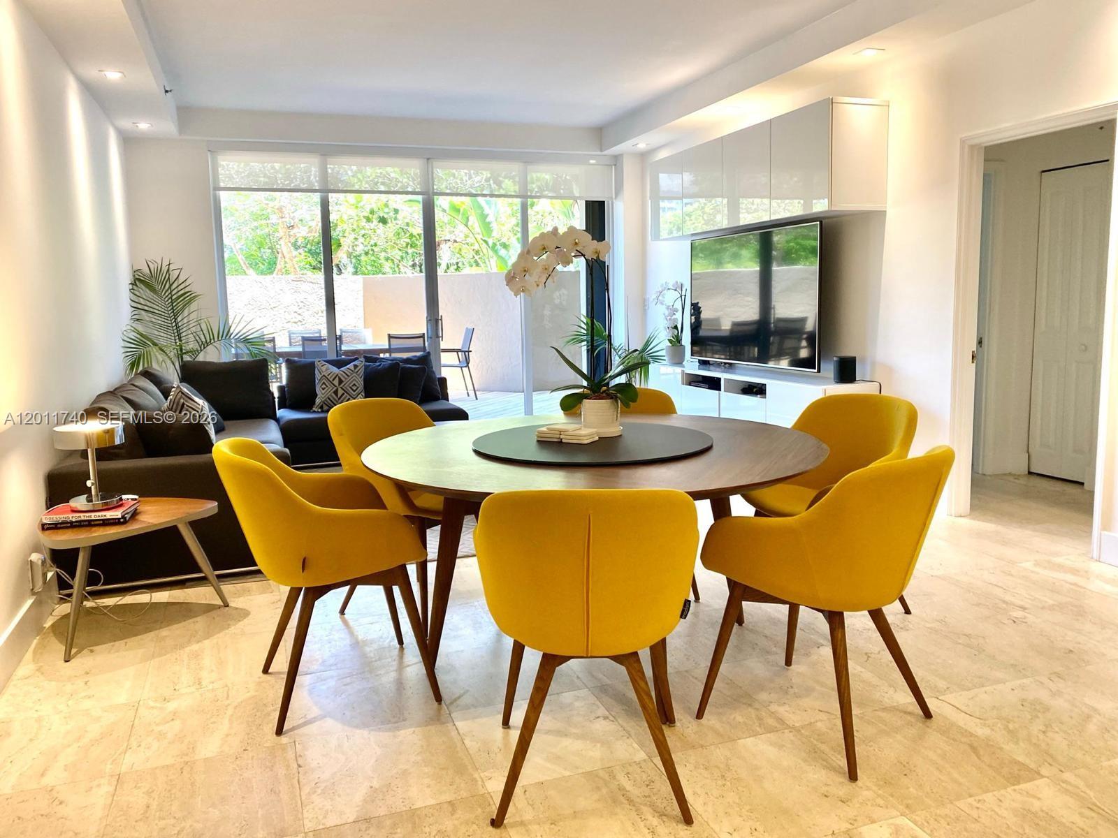 A dining area with a round wooden table and yellow chairs sits before a living room — 251 Crandon Blvd # 139, Key Biscayne FL 33149, KEY BISCAYNE, FL