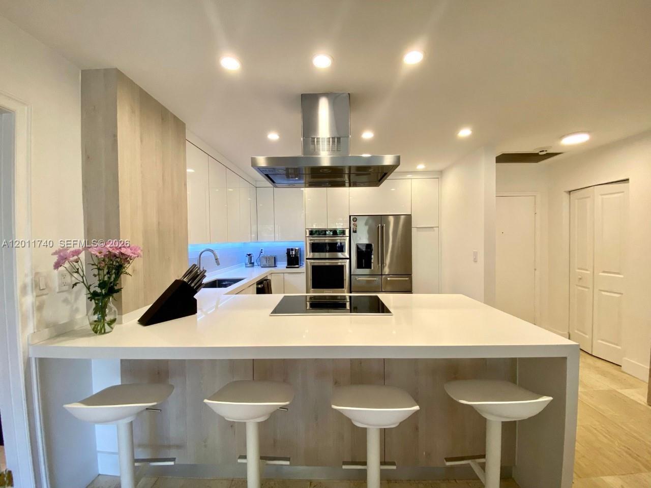 A modern kitchen features white cabinetry, a large island with bar seating, and stainless appliances — 251 Crandon Blvd # 139, Key Biscayne FL 33149, KEY BISCAYNE, FL