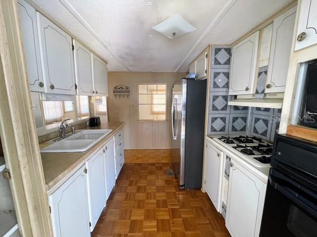 A kitchen features white cabinets, a stainless steel refrigerator, and wood-patterned flooring — 821 TURF, VENICE, FL