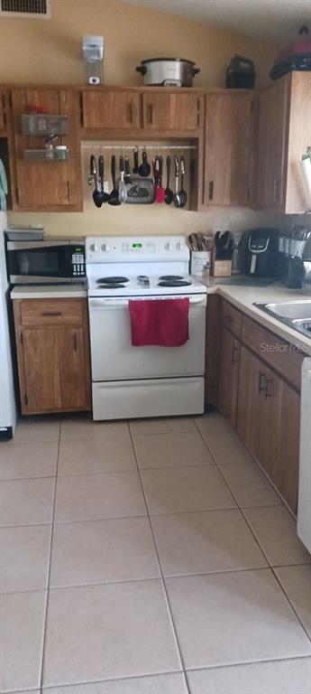A kitchen features wood cabinets, a white electric stove, and light-colored tile flooring — 807 HALEYBURY STREET, PORT CHARLOTTE, FL