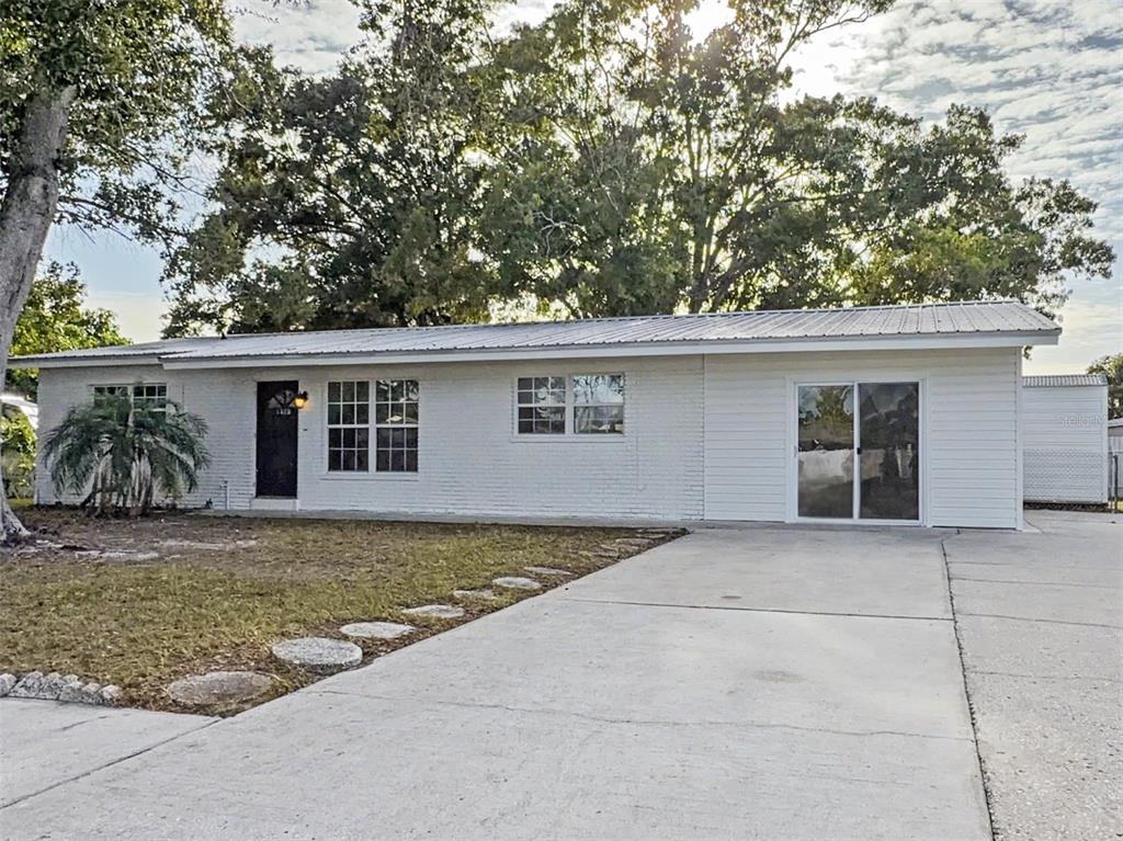 A single-story white house with a metal roof, a concrete driveway, and a front door — 6404 WILLOW BEND PLACE, TAMPA, FL