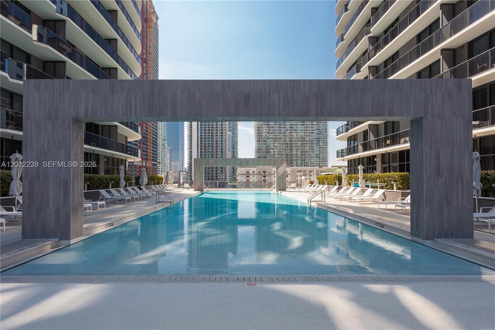 A rectangular swimming pool is framed by two large gray stone arches between apartment buildings — 45 SW 9th St # 1604, Miami FL 33130, MIAMI, FL