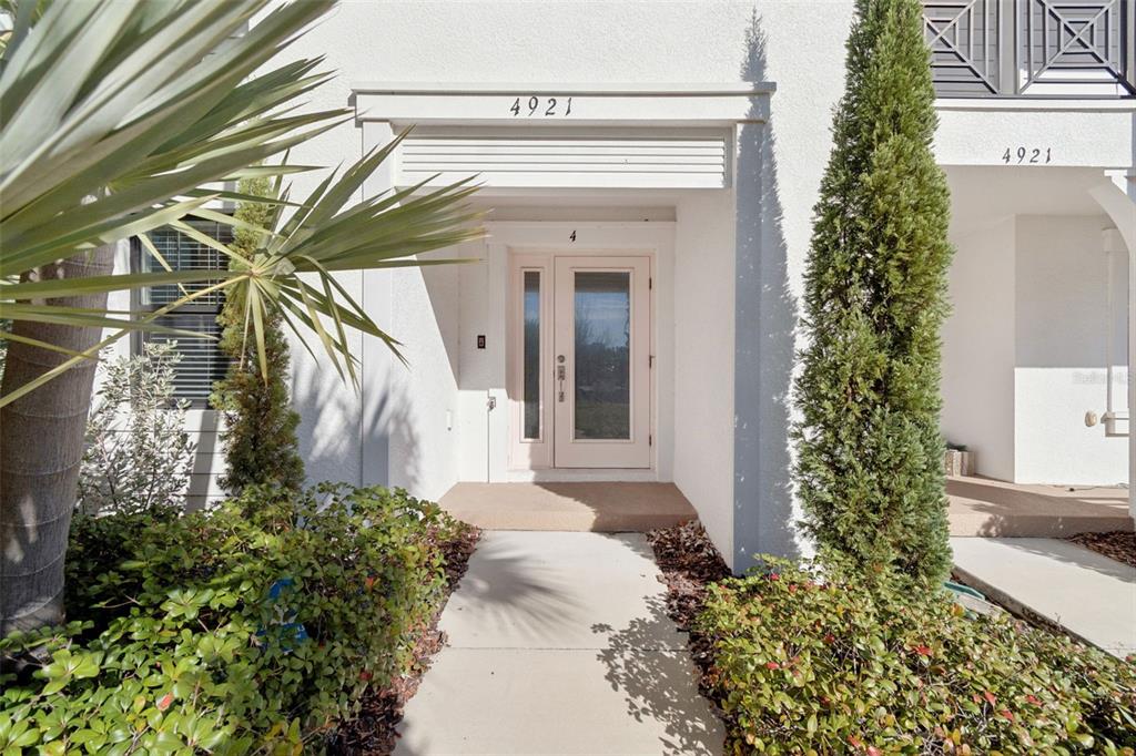 A white exterior entrance features a glass-paneled door, a concrete walkway, and surrounding landscaping — 4921 W PAUL AVENUE UNIT 4, TAMPA, FL