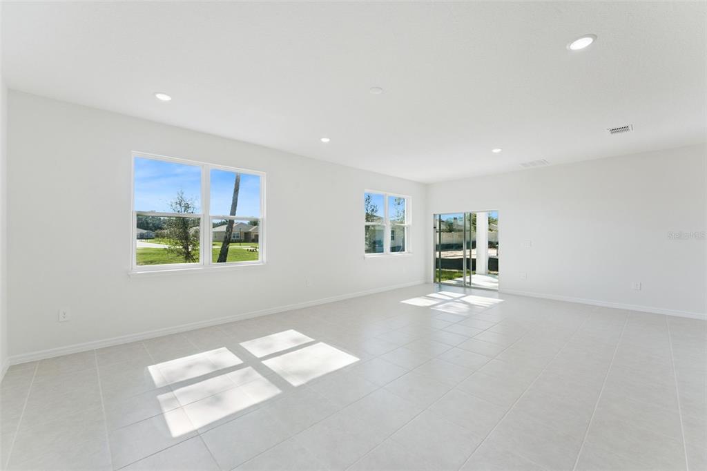 A bright, empty living room features white walls, tiled floors, large windows, and sliding doors — 4300 DARBY COURT, EUSTIS, FL
