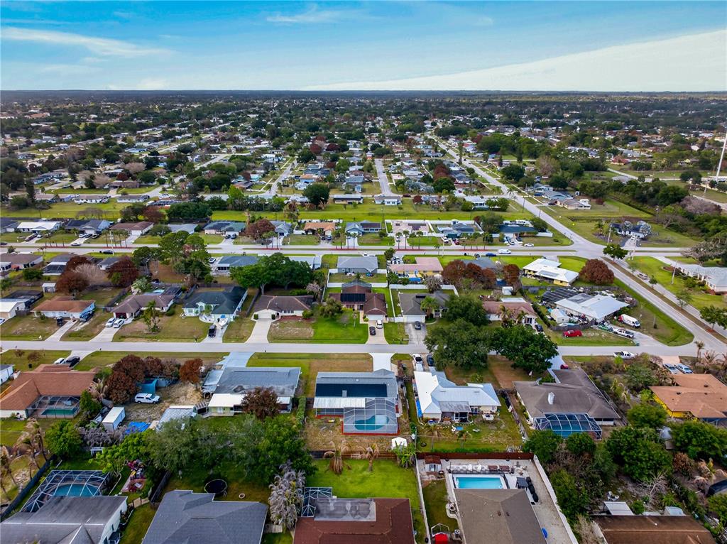 An aerial view shows a suburban neighborhood with single-family homes, swimming pools, and paved streets — 214 SE DUVAL AVENUE, PORT ST LUCIE, FL