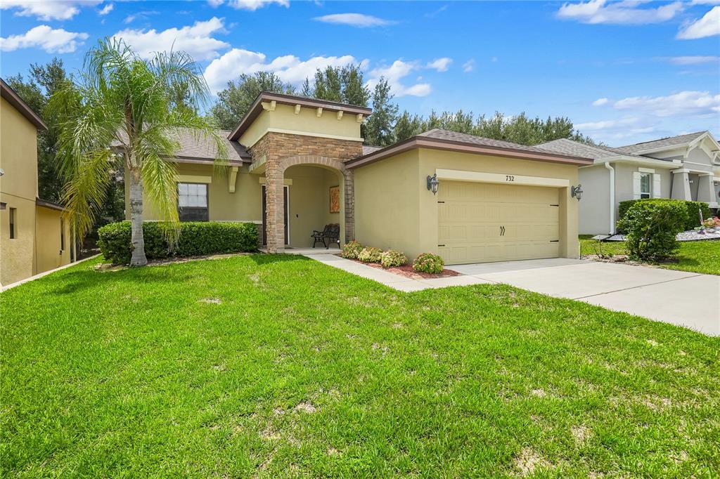 A single-story house with a tan stucco exterior, stone-accented entryway, and a two-car garage — 732 ARBOR POINTE AVENUE, MINNEOLA, FL