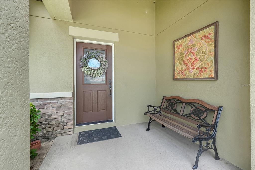 A covered front porch features a brown door with a wreath, a bench, and wall art — 732 ARBOR POINTE AVENUE, MINNEOLA, FL