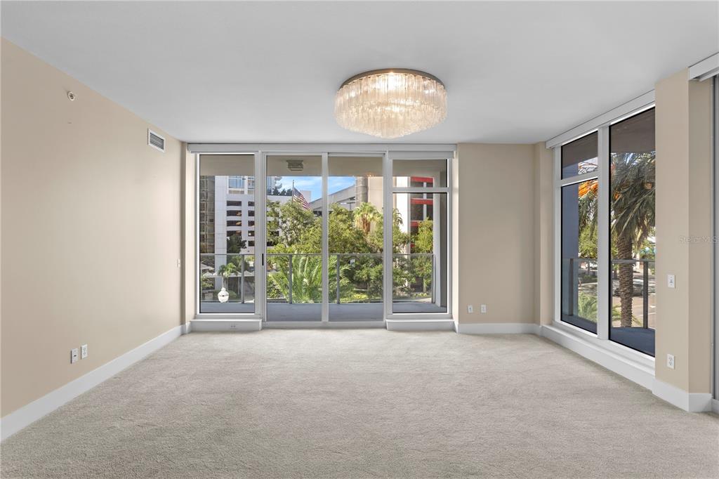 An empty living room features beige carpet, a crystal chandelier, and floor-to-ceiling windows with balcony access — 175 1ST STREET S UNIT 303, ST PETERSBURG, FL