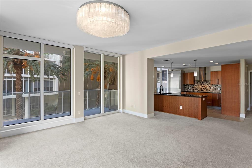 A carpeted living area opens to a kitchen with wood cabinets and a crystal chandelier — 175 1ST STREET S UNIT 303, ST PETERSBURG, FL