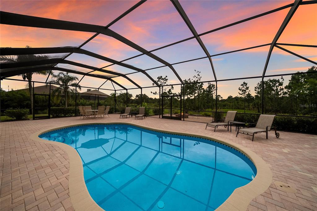A swimming pool with a brick paver deck is enclosed by a screened lanai at sunset — 23327 RED ROBIN PLACE, BRADENTON, FL