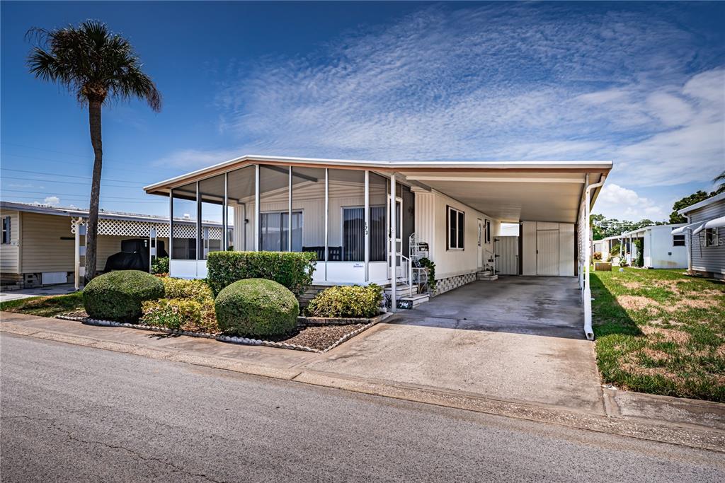 A single-story manufactured home with a screened-in porch, carport, and manicured landscaping — 173 HICKORY GATE DRIVE, PALM HARBOR, FL