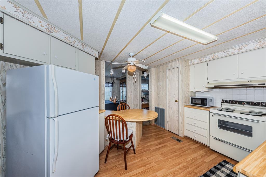 A kitchen with wood-paneled walls, white appliances, a small round table, and light wood flooring — 173 HICKORY GATE DRIVE, PALM HARBOR, FL