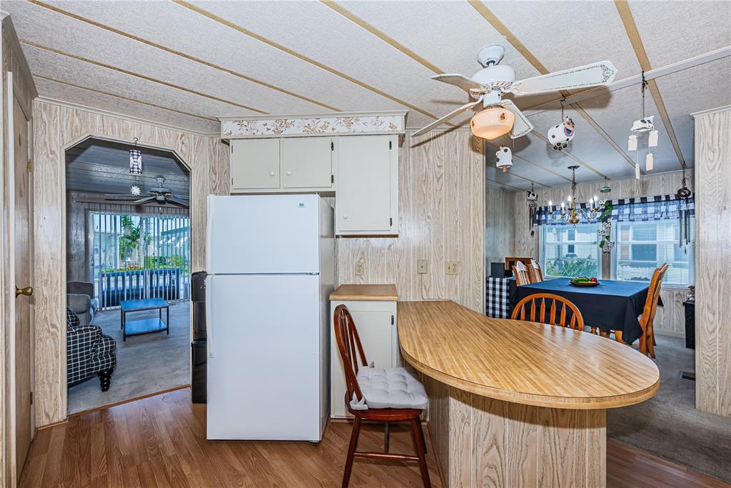 A kitchen with wood-paneled walls, a white refrigerator, a breakfast bar, and a dining area — 173 HICKORY GATE DRIVE, PALM HARBOR, FL