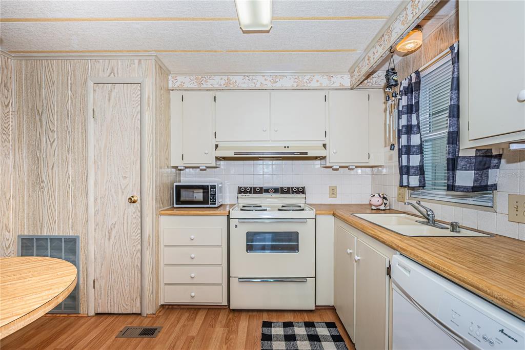 A kitchen features wood-paneled walls, white cabinets, a white stove, and a laminate countertop — 173 HICKORY GATE DRIVE, PALM HARBOR, FL