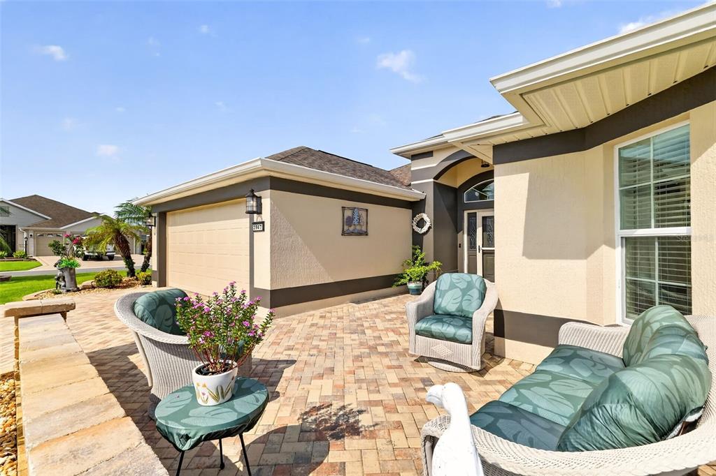 A paved patio features wicker furniture and a small potted plant in front of a house — 2947 RAIN LILY LOOP, THE VILLAGES, FL
