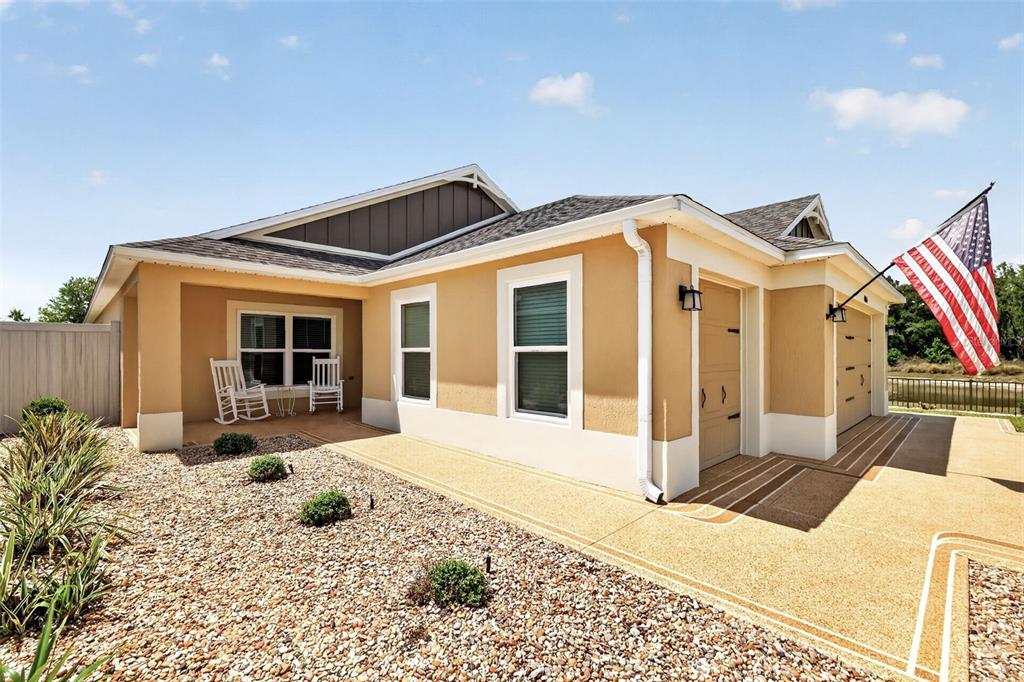 A tan house exterior features a covered porch, gravel landscaping, and an American flag — 4044 MAXWELL TERRACE, THE VILLAGES, FL