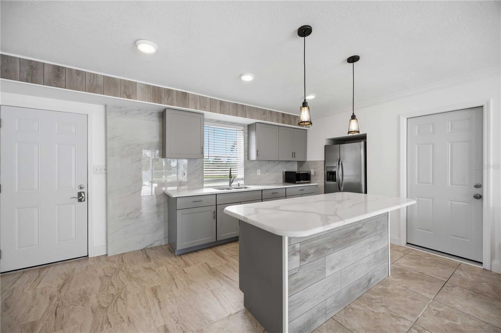 A kitchen features gray cabinets, a marble-look backsplash, a kitchen island, and light tile flooring — 9494 ROSEBUD CIRCLE, PORT CHARLOTTE, FL