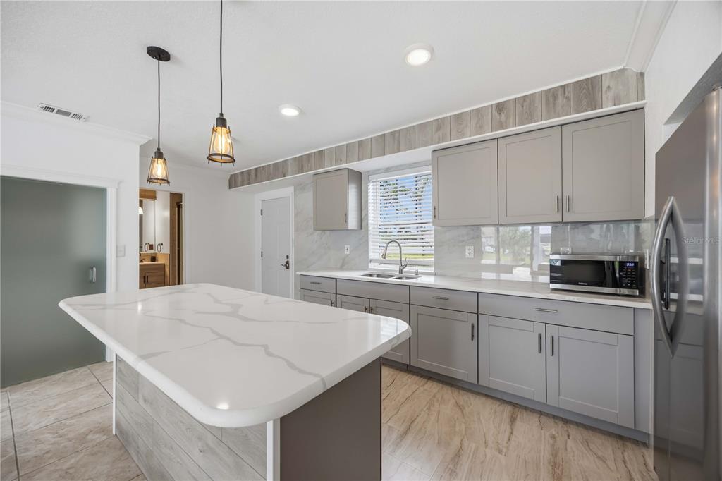 A kitchen features gray cabinets, a white quartz island, and wood-look tile flooring — 9494 ROSEBUD CIRCLE, PORT CHARLOTTE, FL