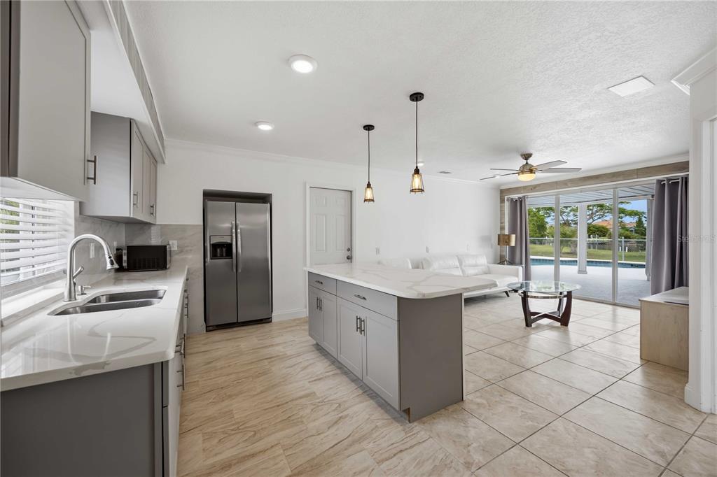 A kitchen with gray cabinets and a marble island opens into a living room area — 9494 ROSEBUD CIRCLE, PORT CHARLOTTE, FL