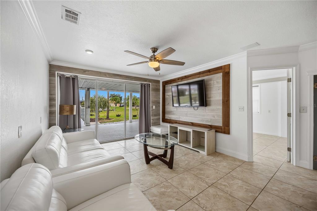 A living room with tile floors, a white sofa, a glass coffee table, and wood-paneled walls — 9494 ROSEBUD CIRCLE, PORT CHARLOTTE, FL