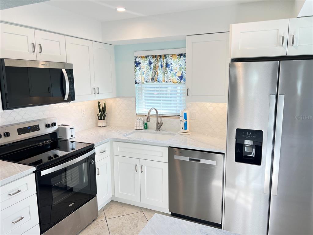 A kitchen features white cabinets, stainless steel appliances, a tiled backsplash, and light countertops — 6154 MIDNIGHT PASS ROAD UNIT B11, SARASOTA, FL