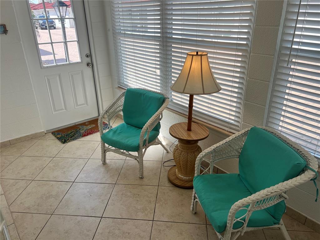 A sunroom features two white wicker chairs with teal cushions, a lamp, and tiled flooring — 6154 MIDNIGHT PASS ROAD UNIT B11, SARASOTA, FL