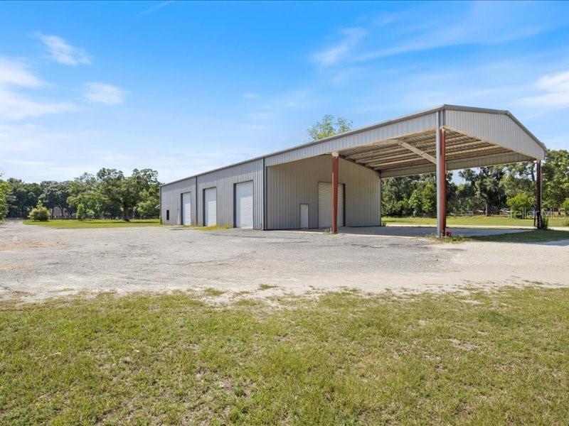 A large metal warehouse building features multiple garage doors and an attached open-air carport — 22429 S US HIGHWAY 441, HIGH SPRINGS, FL