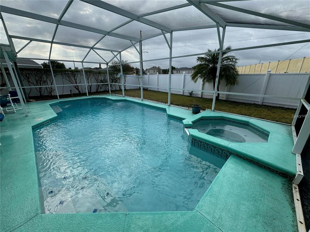 A swimming pool and attached spa are enclosed within a screened lanai with green decking — 702 SONJA CIRCLE, DAVENPORT, FL