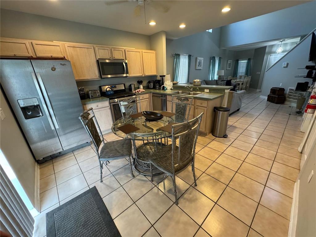 A kitchen with light wood cabinets, stainless steel appliances, and a glass-topped dining table — 702 SONJA CIRCLE, DAVENPORT, FL