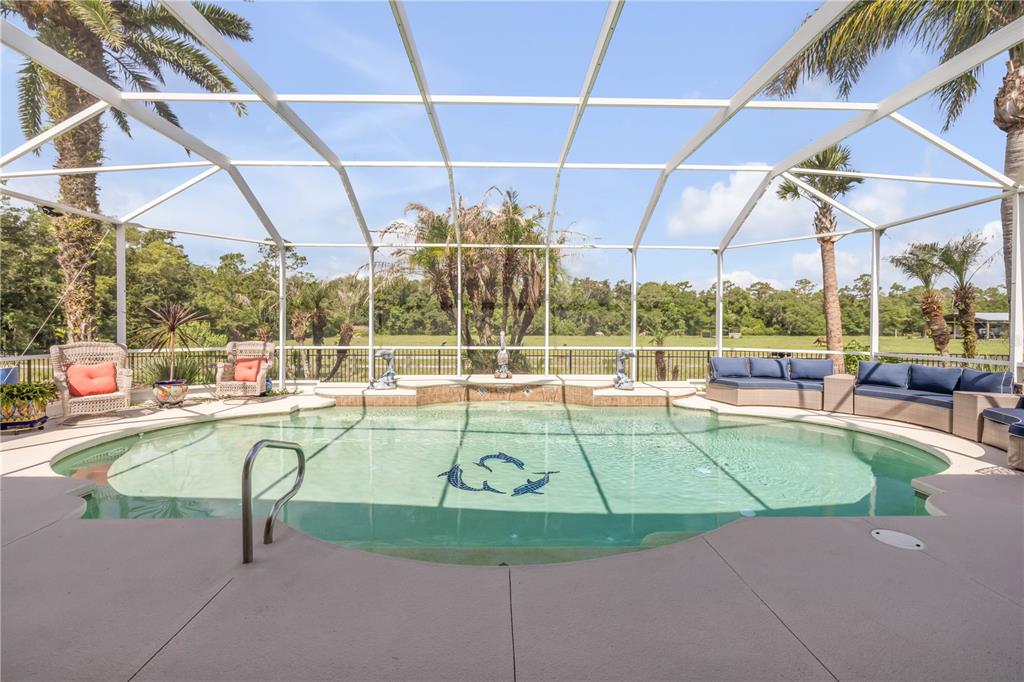 A screened-in swimming pool with a patio, outdoor seating, and palm trees in the background — 3604 MARIBELLA DRIVE, NEW SMYRNA BEACH, FL