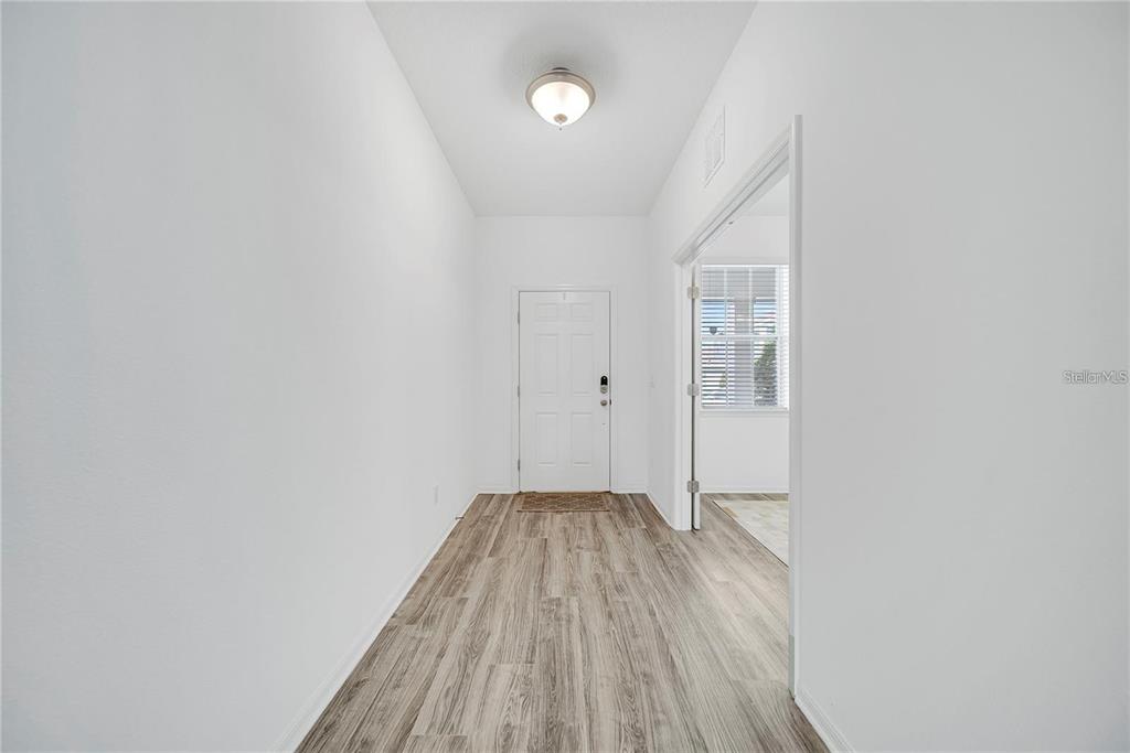 A bright entryway features white walls, a flush-mount light fixture, and wood-look flooring — 6460 MAKRUT LIME DRIVE, WINTER GARDEN, FL