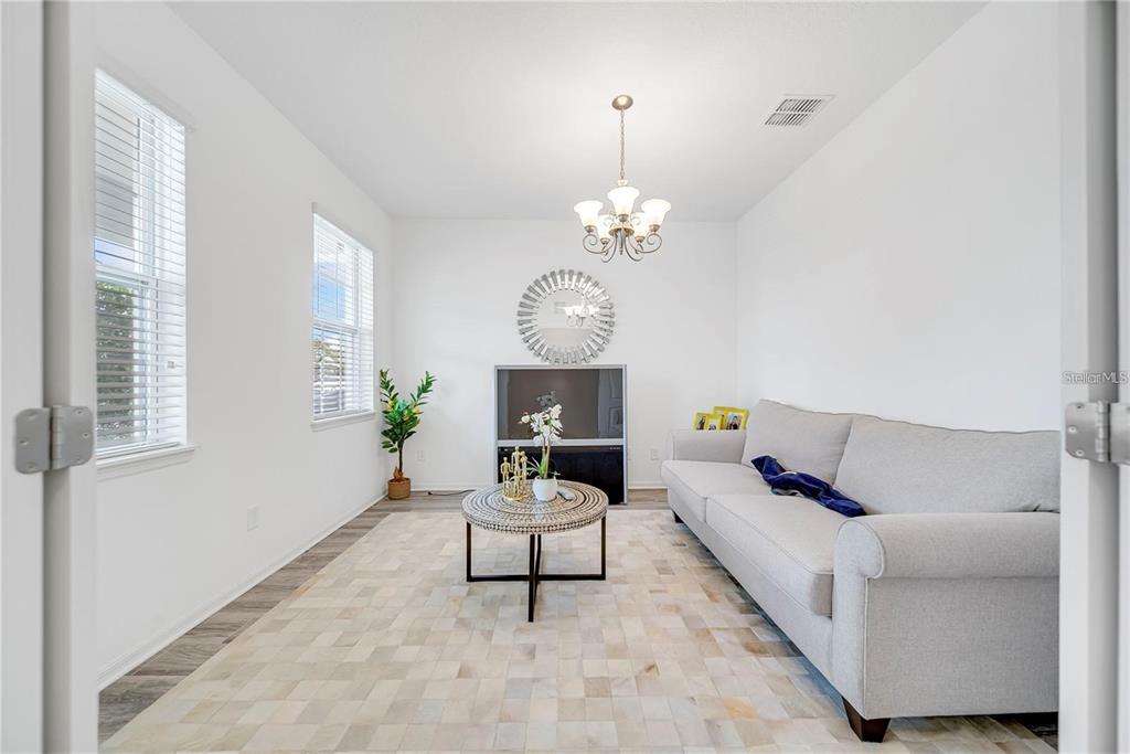 A bright living room features a light gray sofa, a round coffee table, and a chandelier — 6460 MAKRUT LIME DRIVE, WINTER GARDEN, FL
