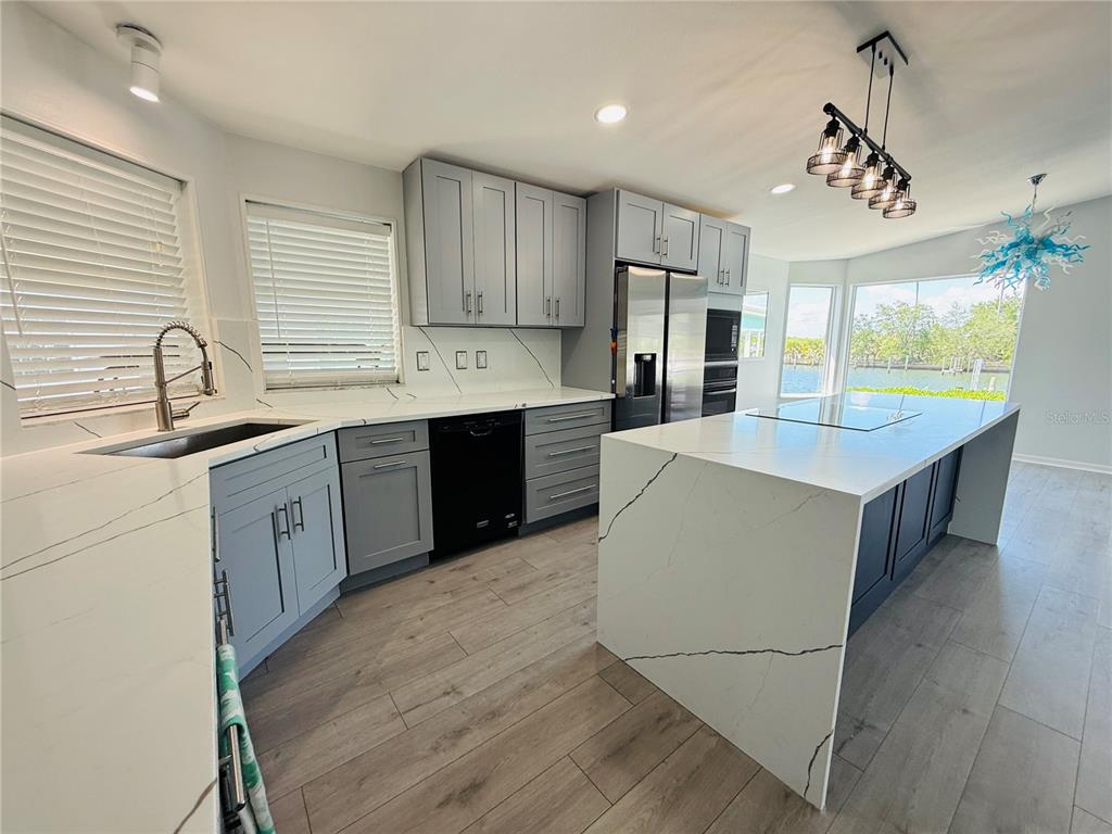 A modern kitchen features gray cabinets, white marble-look countertops, a large island, and water views — 4851 W GANDY BOULEVARD UNIT 5C, TAMPA, FL