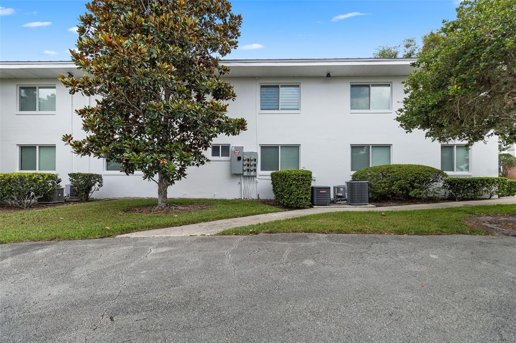 The exterior of a two-story white apartment building features a large tree and landscaping — 1140 S ORLANDO AVENUE UNIT E11, MAITLAND, FL