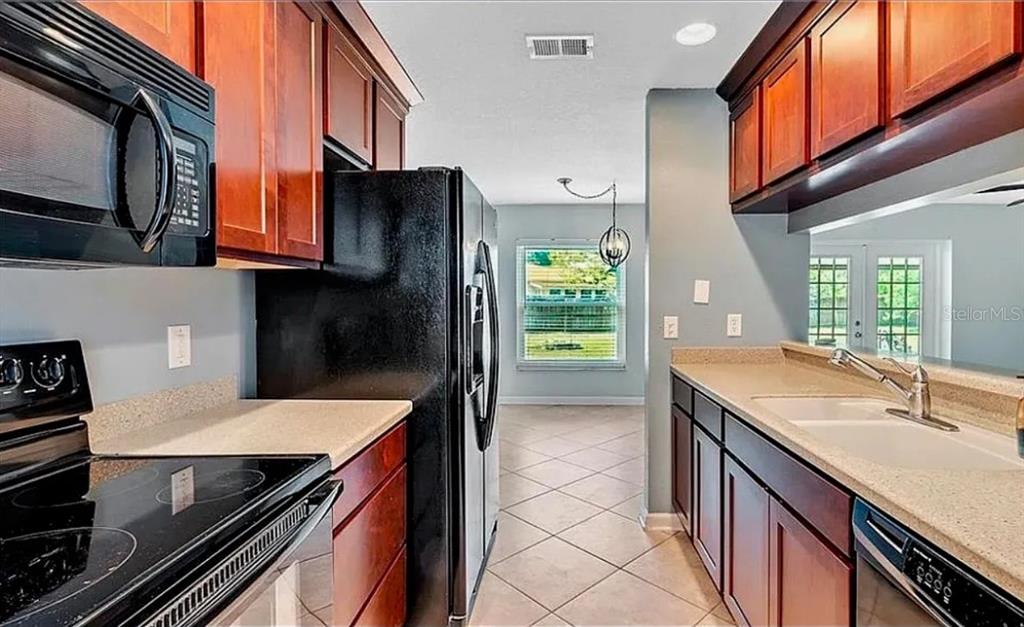 A kitchen features dark wood cabinets, black appliances, light countertops, and a tile floor — 120 BENT OAK COURT, SANFORD, FL