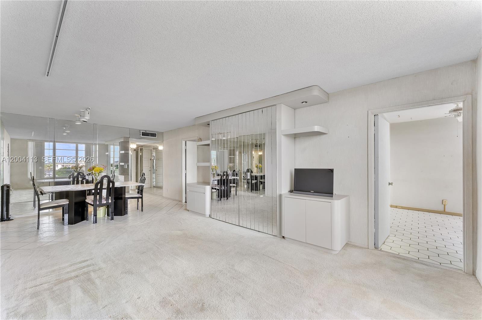 A living room with beige carpet, mirrored wall panels, and an adjacent dining area — 2661 S Course Dr # 805, Pompano Beach FL 33069, POMPANO BEACH, FL
