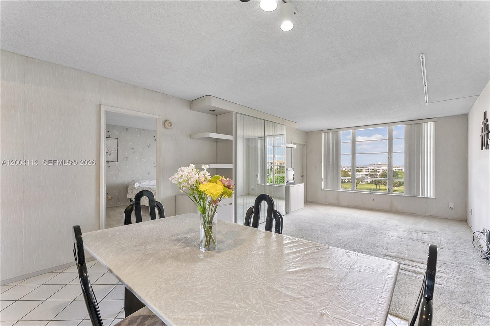 A dining area with a table and chairs opens into a carpeted living room — 2661 S Course Dr # 805, Pompano Beach FL 33069, POMPANO BEACH, FL