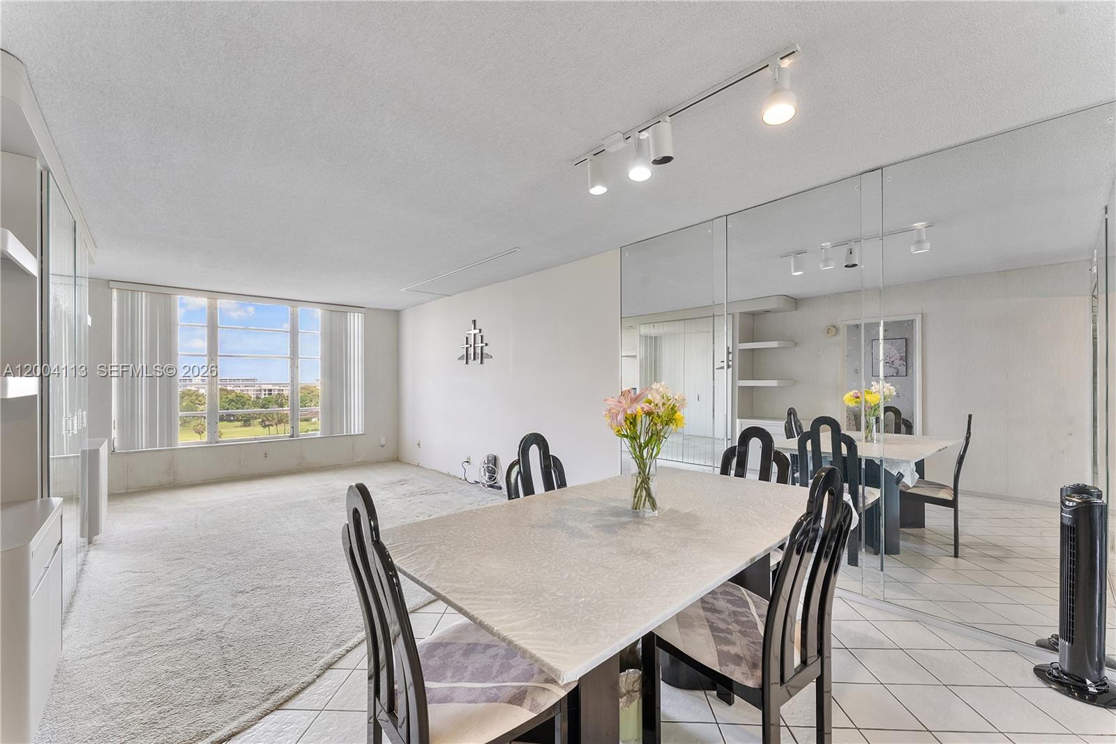 A dining area with a table and chairs sits adjacent to a carpeted living space — 2661 S Course Dr # 805, Pompano Beach FL 33069, POMPANO BEACH, FL