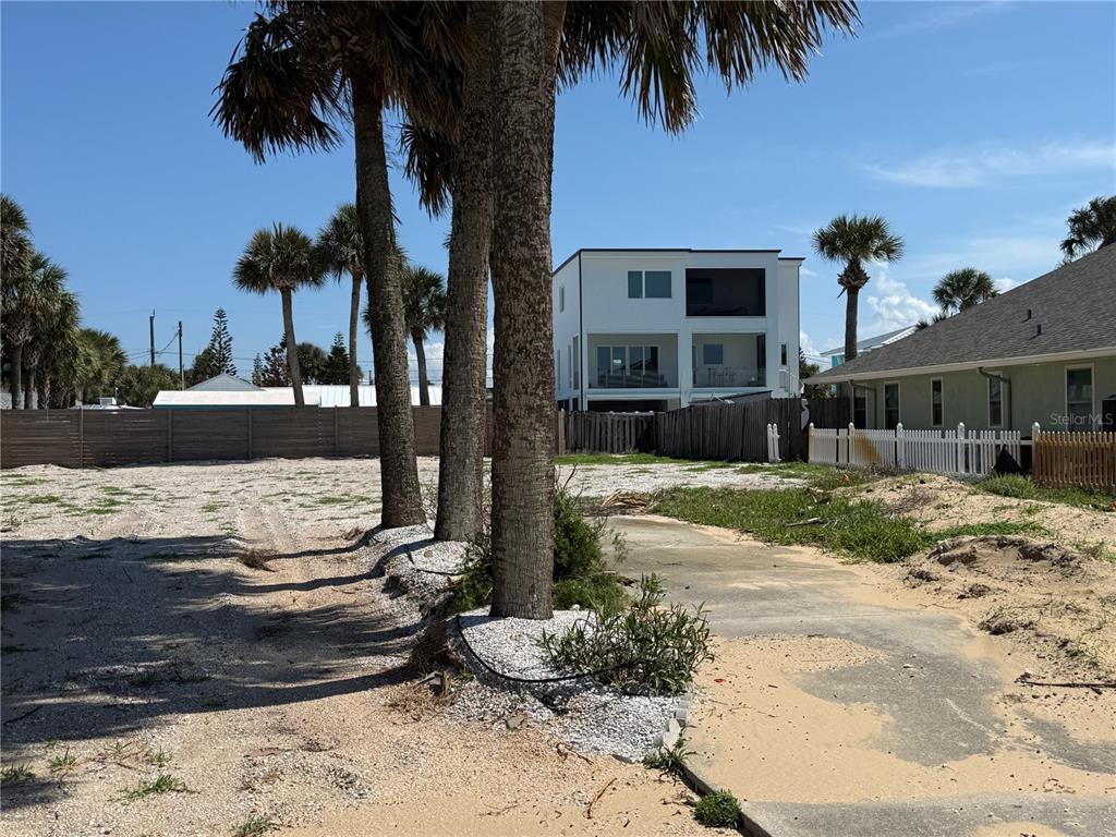 A vacant sandy lot features several palm trees and a concrete driveway near neighboring houses — 0 DUE EAST STREET, NEW SMYRNA BEACH, FL