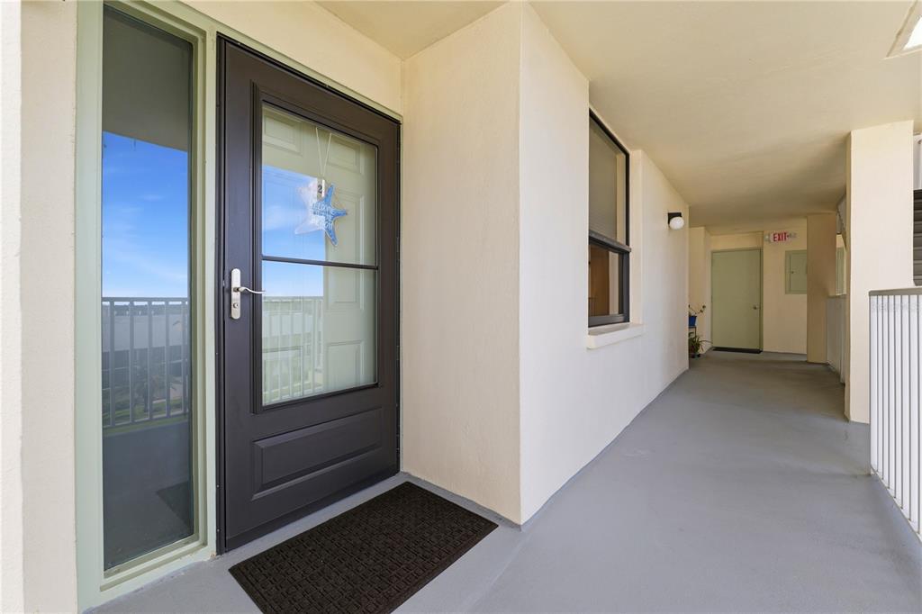 A dark front door with a glass storm door sits on a covered outdoor walkway — 300 WOODETTE DRIVE UNIT 602, DUNEDIN, FL