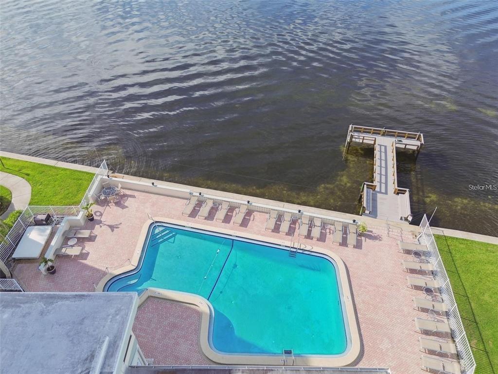 An aerial view shows a swimming pool on a patio next to a wooden dock — 300 WOODETTE DRIVE UNIT 602, DUNEDIN, FL