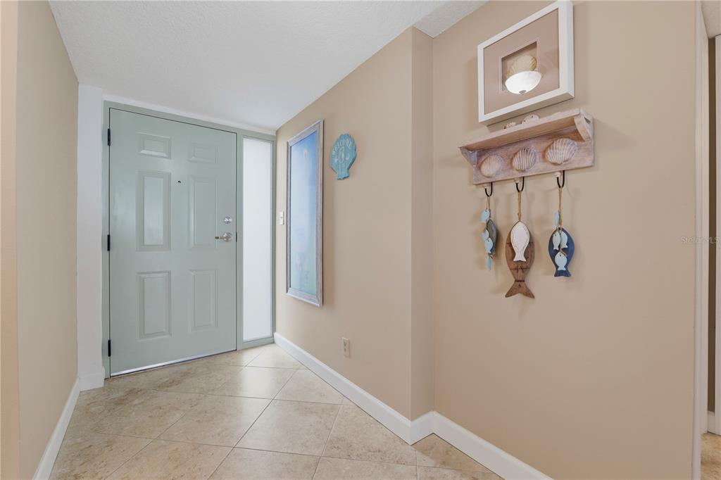 An entryway features light-colored tile flooring, a pale green door, and coastal-themed wall decor — 300 WOODETTE DRIVE UNIT 602, DUNEDIN, FL