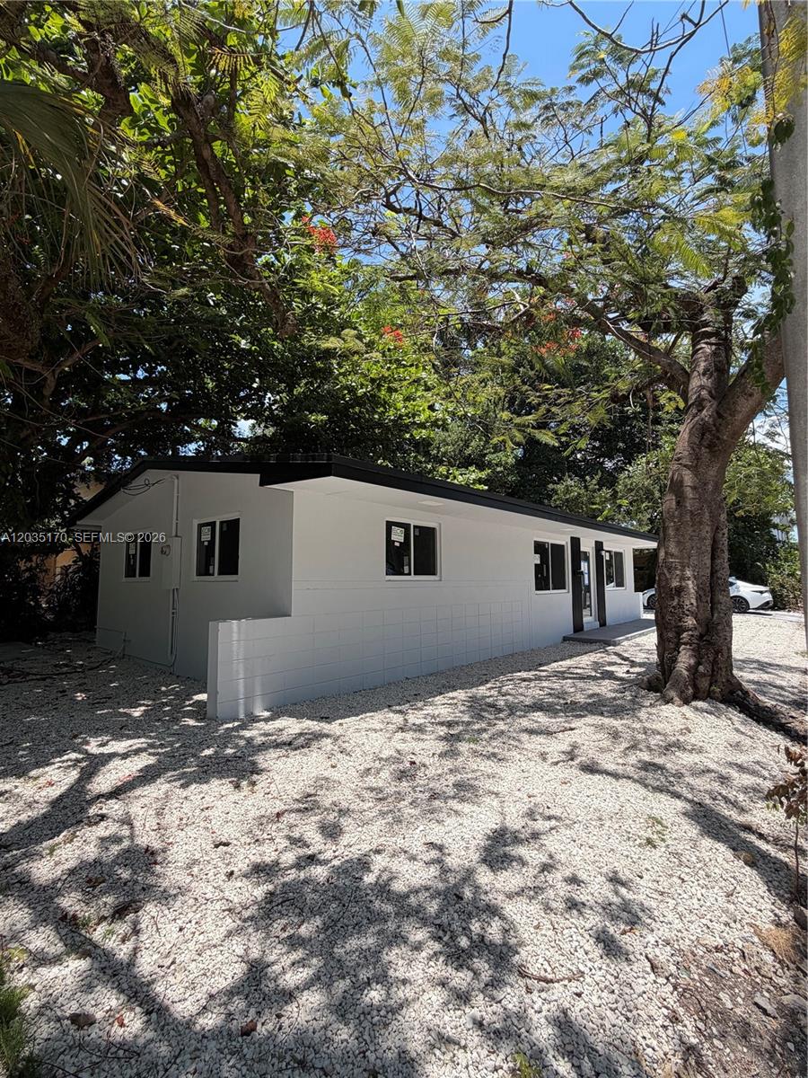 A white, single-story house with a gravel yard and large trees under a blue sky — 3220 Plaza St # 3220, Miami FL 33133, MIAMI, FL