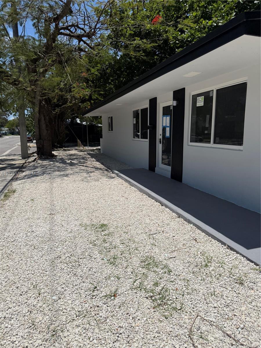 The exterior of a white building features a gravel yard and a covered concrete walkway — 3220 Plaza St # 3220, Miami FL 33133, MIAMI, FL