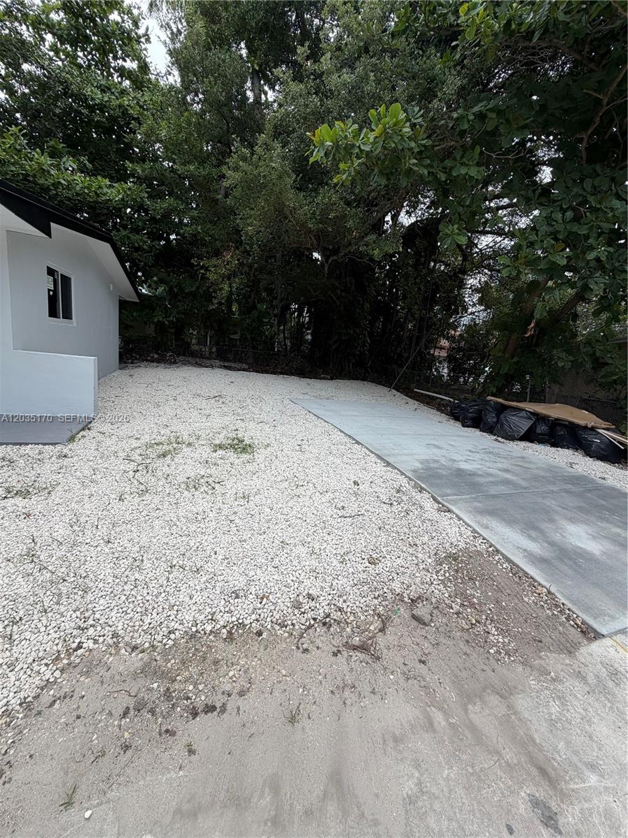 A gravel yard sits beside a concrete driveway next to a white house exterior — 3220 Plaza St # 3220, Miami FL 33133, MIAMI, FL