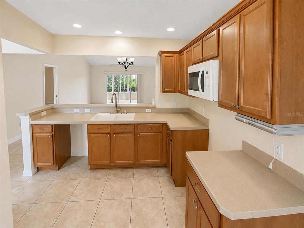 A kitchen features wood cabinets, beige countertops, tile flooring, and a white microwave — 2251 EDMONTON PLACE, THE VILLAGES, FL