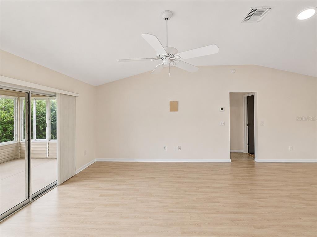 An empty living room features light wood-look flooring, a ceiling fan, and sliding glass doors — 2251 EDMONTON PLACE, THE VILLAGES, FL