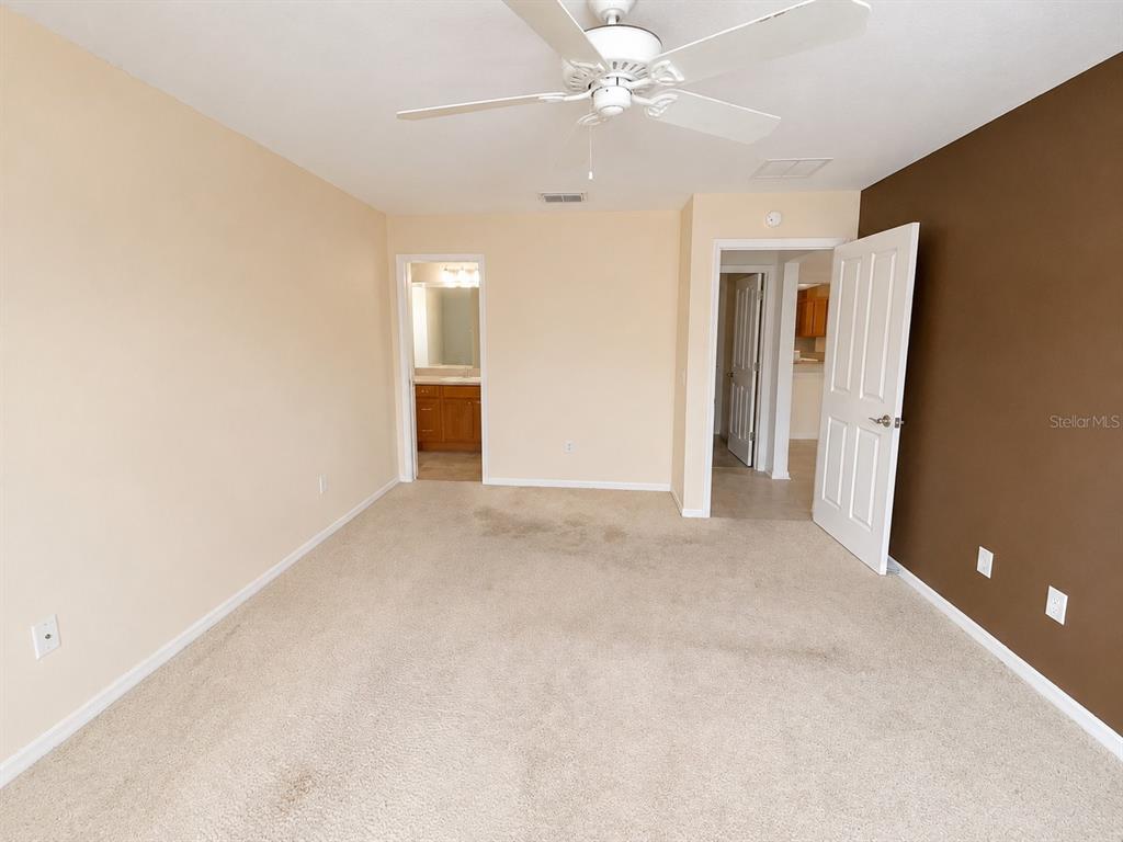 An empty bedroom features beige carpet, a ceiling fan, and a brown accent wall — 2251 EDMONTON PLACE, THE VILLAGES, FL